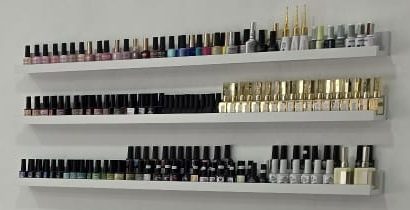 Detalle de tres estantes con esmaltes de uñas de muchos colores