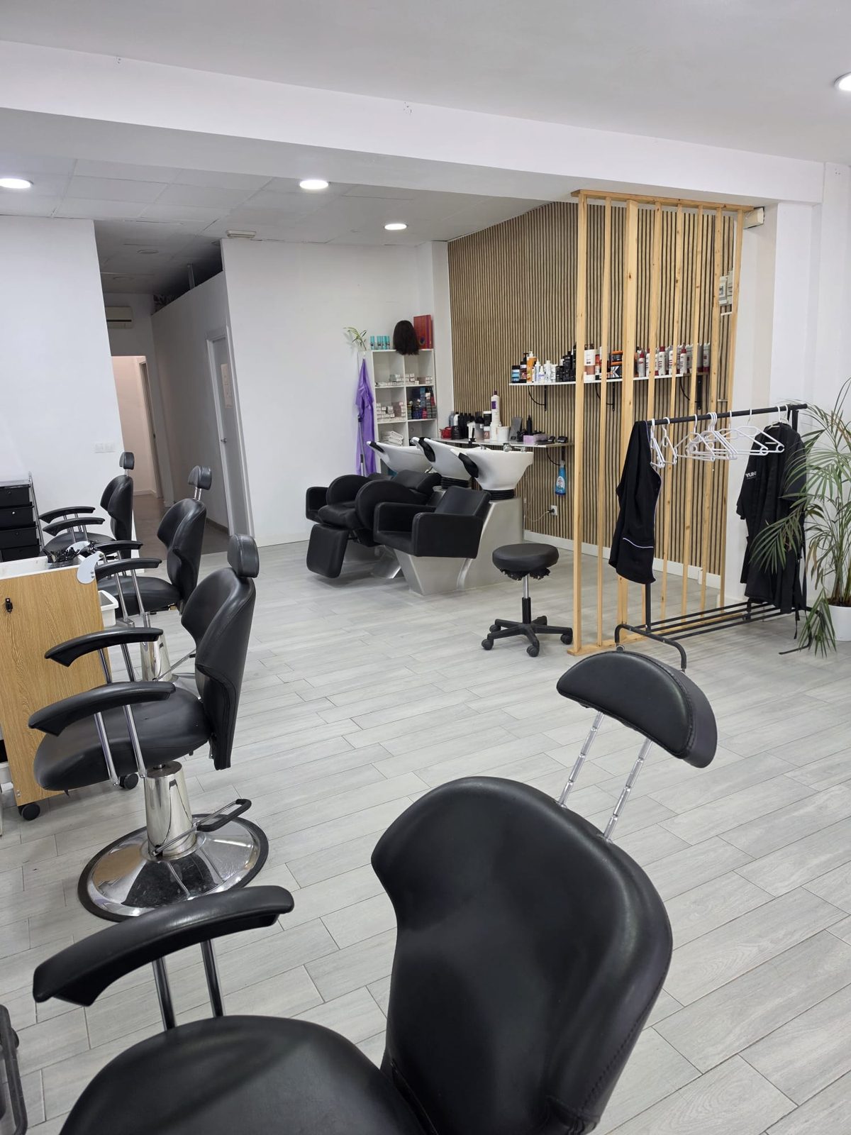 Zona de lavado con tres lavacabezas blancos y sillones negros, junto a una pared de listones de madera con estantes de productos