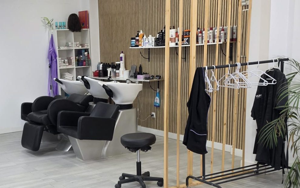 Tres lavacabezas blancos con sillones negros junto a una pared de listones de madera con estantes de productos